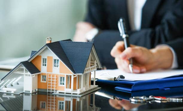 Lawyer reviewing property documents with a house model on desk.